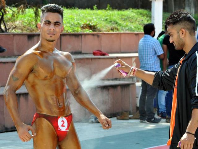 A man applying body spray on a contender for the 'Mr. Jammu Body Building Competition'’. (Nitin Kanotra / HT)