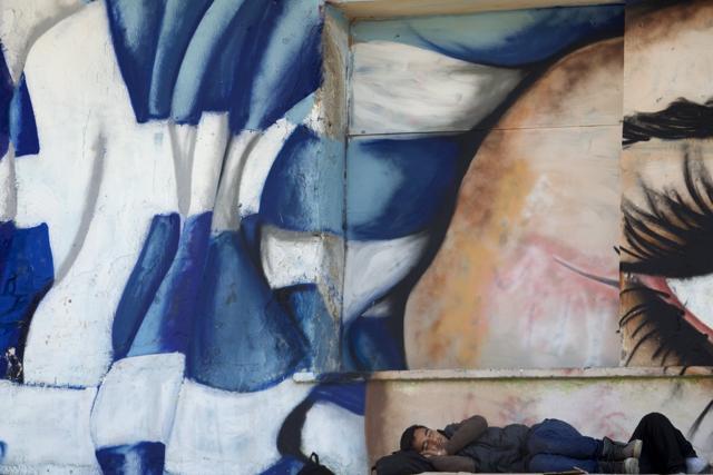 A migrant sleeps in front of a graffiti covered wall depicting a face and the Greek national flag at the port of Mytilene on the island of Lesbos, Greece, on October 6, 2015. (Reuters Photo) A migrant sleeps in front of a graffiti covered wall depicting a face and the Greek national flag at the port of Mytilene on the island of Lesbos, Greece, on October 6, 2015. (Reuters Photo)