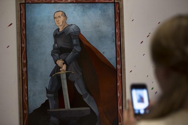 A woman takes a picture of an artwork depicting Russian President Vladimir Putin as King Arthur during the "Putin Universe" exhibition in Moscow. (AP Photo)