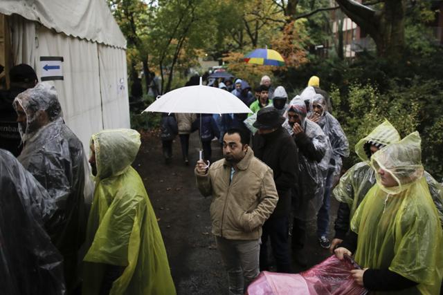 Protected against rain migrants and refugees wait in front of a tent for food at the central registration center for refugees and asylum seekers LaGeSo (Landesamt fuer Gesundheit und Soziales - State Office for Health and Social Affairs) in Berlin. (AP)