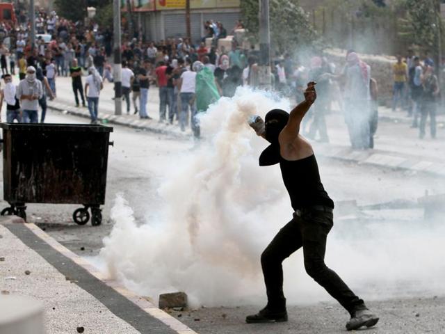 A Palestinian youth throws a tear gas canister back towards Israeli security forces (unseen) during clashes at the main entrance of the West Bank town of Bethlehem. (AFP Photo)