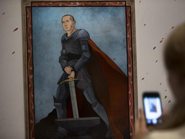 A woman takes a picture of an artwork depicting Russian President Vladimir Putin as King Arthur during the "Putin Universe" exhibition in Moscow. (AP Photo)