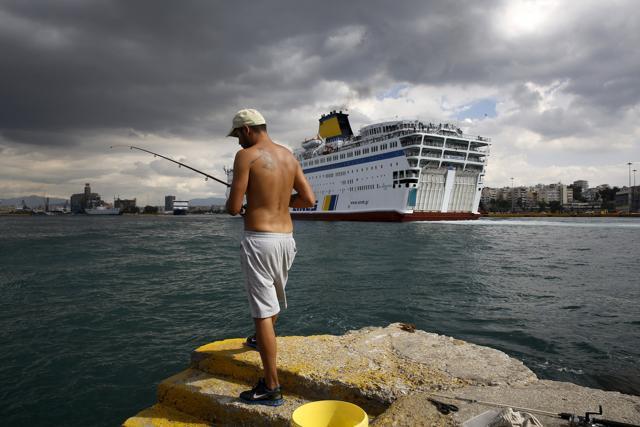 A local bearing a tattoo of a Spartan warrior fishes as the passenger ferry Eleftherios Venizelos, carrying over 2,500 refugees and migrants from the island of Lesbos, arives at the port of Piraeus, near Athens. (REUTERS) A local bearing a tattoo of a Spartan warrior fishes as the passenger ferry Eleftherios Venizelos, carrying over 2,500 refugees and migrants from the island of Lesbos, arives at the port of Piraeus, near Athens. (REUTERS)