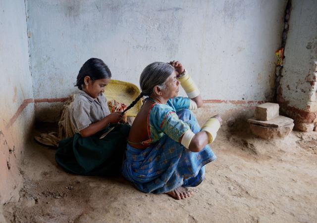 Lambadi tribal child K Sravanthi, who lost her father in a road accident, braids the hair of her grandmother at her home. (AFP) Lambadi tribal child K Sravanthi, who lost her father in a road accident, braids the hair of her grandmother at her home. (AFP)