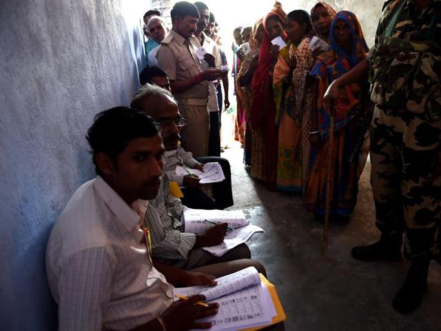 Election officials (L) sit at a voting centre as voters queue to cast their ballots in the village of Banbira in Samastipur district. (AFP)