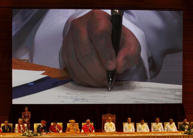 The hand of a leader of an armed ethnic group is seen on a screen as he signs the Nationwide Ceasefire Agreement (NCA) as Myanmar's President Thein Sein (6th right), government officials, ethnic rebel groups and international witnesses sit below during the signing ceremony of the NCA in Naypyitaw, Myanmar. (REUTERS) The hand of a leader of an armed ethnic group is seen on a screen as he signs the Nationwide Ceasefire Agreement (NCA) as Myanmar's President Thein Sein (6th right), government officials, ethnic rebel groups and international witnesses sit below during the signing ceremony of the NCA in Naypyitaw, Myanmar. (REUTERS)