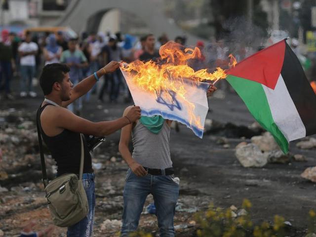 A Palestinian protester burns a replica Israeli flag as another holds a Palestinian flag during clashes with the Israeli troops near the Jewish settlement of Bet El, near the West Bank city of Ramallah. (Reuters Photo)
