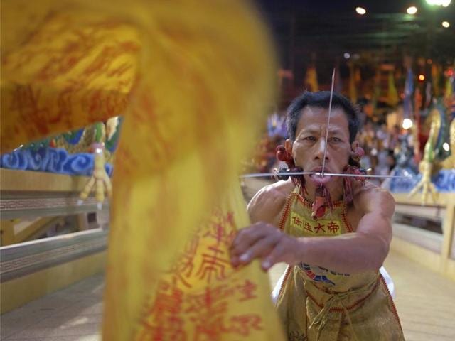 A devotee to the Chinese shrine of Ban Tha Rue waves a ceremonial flag after having his face pierced prior to a street procession. During the nine-day festival in Phuket Town , residents observe a strict vegetarian or vegan diet that is believed to cleanse the body and grant merit. (AP Photo/David Longstreath) (AP)