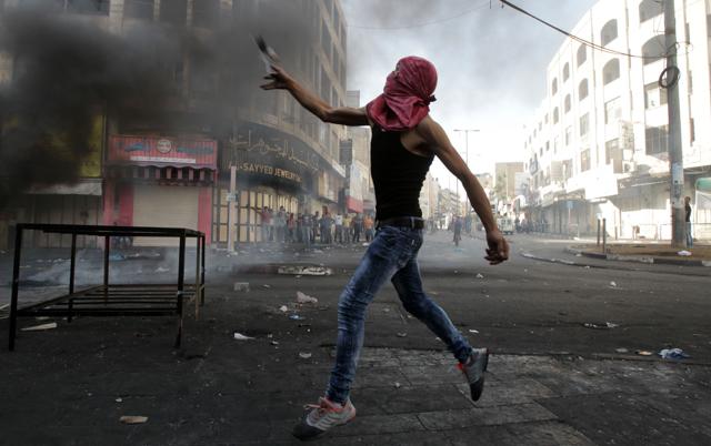 A masked Palestinian protester throws stones during clashes with Israeli security forces in the occupied West Bank city of Hebron, on October 22, 2015, following the funeral of Hashem al-Azzeh, who died after suffocating by tear gas fired by Israeli security forces during clashes close to the Israeli settlement of Tal Rumeida. (AFP Photo)