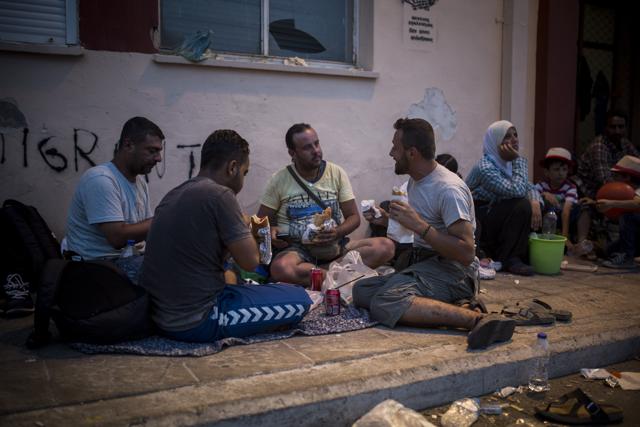 In this photo taken on Monday, Sept. 7, 2015, Mohammed al-Haj from Syria, right, eats a sandwich with friends as he waits to be registered and issued travel documents by local authorities at the port of Mytilene, on the northeastern island of Lesbos, Greece. (AP Photo) In this photo taken on Monday, Sept. 7, 2015, Mohammed al-Haj from Syria, right, eats a sandwich with friends as he waits to be registered and issued travel documents by local authorities at the port of Mytilene, on the northeastern island of Lesbos, Greece. (AP Photo)