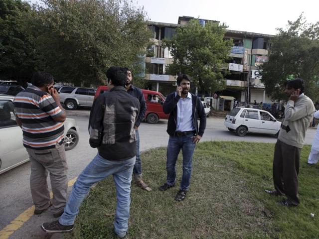 Men stand on a road divider after vacating their office buildings following an earthquake in Islamabad, Pakistan. (REUTERS)
