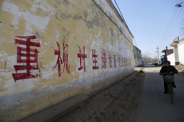 A resident rides a bicycle past a slogan on the wall which partially read "pay attention to One Child Policy and seek developments", at a village in Handan, Hebei province, China. (Reuters Photo)