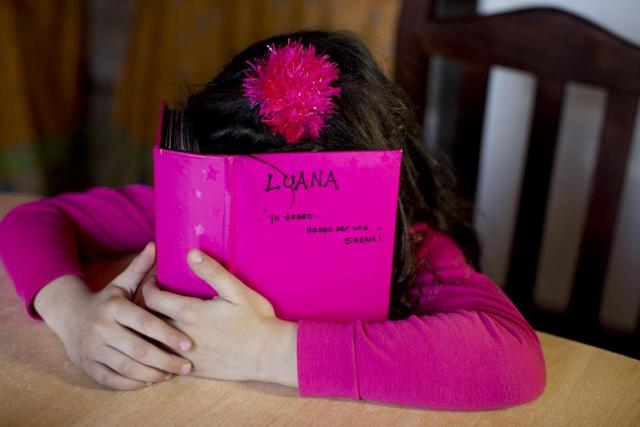 Luana hides behind her photo album at her home in Merlo, Argentina. (AP)