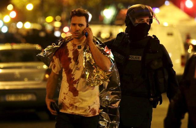 A French policeman assists a blood-covered victim near the Bataclan concert hall following attacks in Paris. (REUTERS)