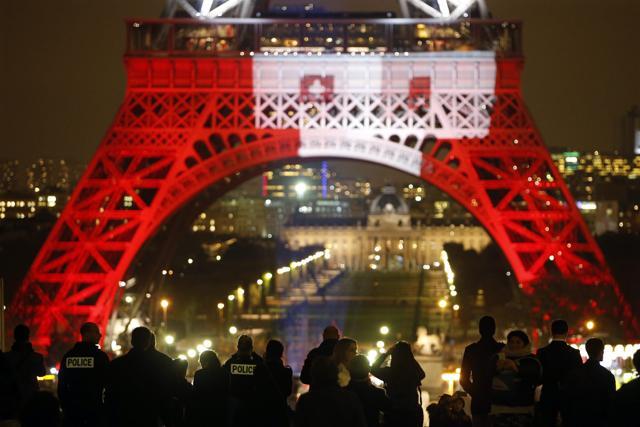 French police stand guard as people gather to look at the Eiffel Tower that is lit with the blue, white and red colours of the French flag in Paris. (REUTERS) French police stand guard as people gather to look at the Eiffel Tower that is lit with the blue, white and red colours of the French flag in Paris. (REUTERS)
