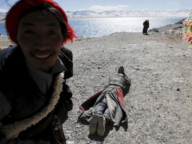 A Tibetan looks at the camera as other one prostrates himself at the lake. (REUTERS)