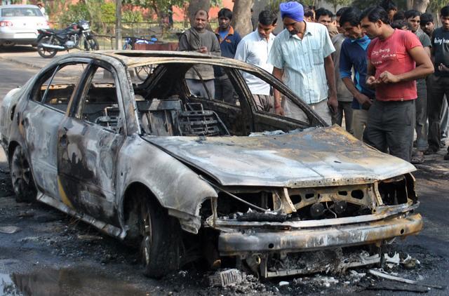 Residents of teh area looking at the car which was caught fire in Mohali on Tuesday. (HT Photo)
