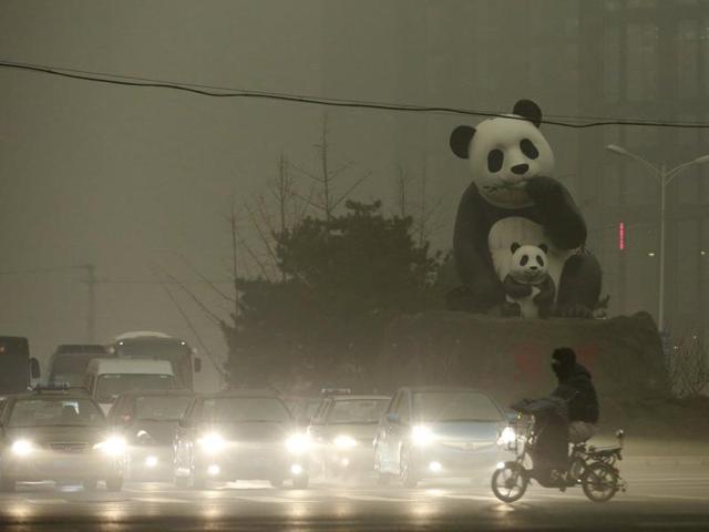 A resident rides an electric bicycle across a street amid heavy smog as vehicles wait for a traffic light next to a statue of pandas, a landmark of the Wangjing area in Beijing. (REUTERS Photo)