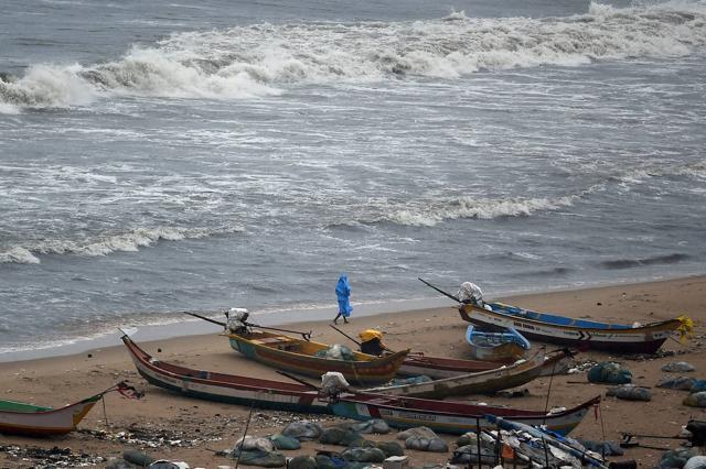 A fisherman walks near boats during heavy rain near Marina Beach in Chennai. (PTI) A fisherman walks near boats during heavy rain near Marina Beach in Chennai. (PTI)
