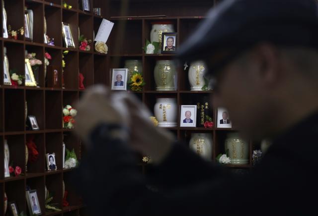 In this Nov. 25, 2015 photo, the funeral shop owner Cheng Chi-kit holds incense sticks at a funeral parlor with a wall of temporary storage niches for cremated remains in the background in Hong Kong. (AP) In this Nov. 25, 2015 photo, the funeral shop owner Cheng Chi-kit holds incense sticks at a funeral parlor with a wall of temporary storage niches for cremated remains in the background in Hong Kong. (AP)