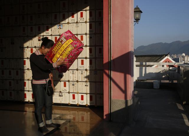 In this Nov. 28 photo, a woman prays as she holds a package of paper money intended to be burned as offerings to her dead father with a wall of niches for cremated remains in the background at a private columbarium in Hong Kong. (AP) In this Nov. 28 photo, a woman prays as she holds a package of paper money intended to be burned as offerings to her dead father with a wall of niches for cremated remains in the background at a private columbarium in Hong Kong. (AP)