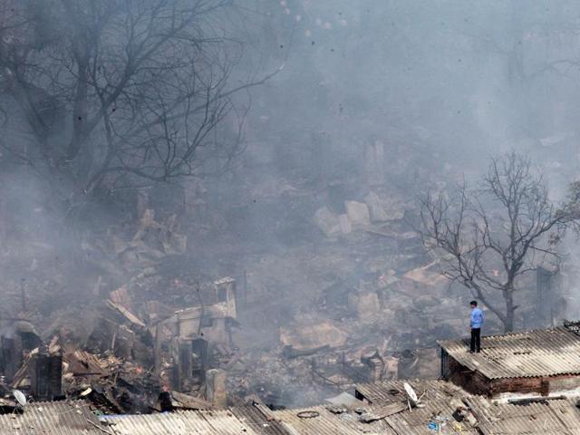 A man stands atop a roof surveying the site at Damu Nagar where a major fire broke out on Monday. The blaze, which spread across 12 acres, gutted around 2,000 shanties, leaving nearly 10,000 people homeless. (Pratham Gokhale/ HT Photo)