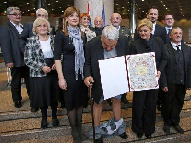 A combination of pictures made on December 8, 2015 shows Croatia's leading rights group chief Ivan Zvonimir Cicak's (L) looking down and pulling up his trousers after they fell down while posing for a photo with Croatian President Kolinda Grabar-Kitarovic (R) on December 8, 2015 in Zagreb.(AFP)