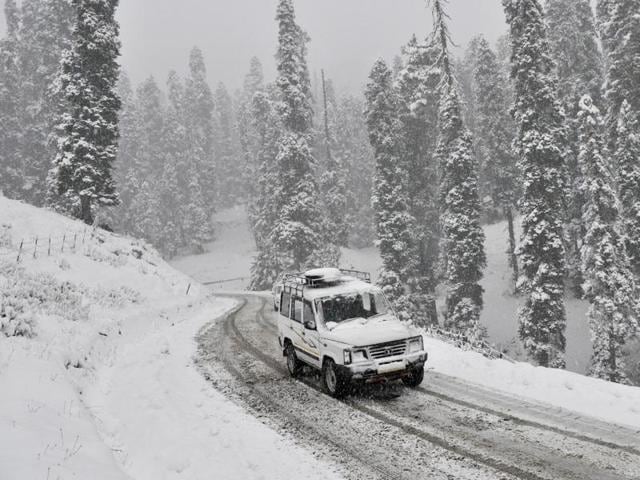 A vehicle drives past a snow-covered Gulmarg-Tangmarg road, 38 kilometers from Srinagar on Thursday. (Waseem andrabi/HT Photo)