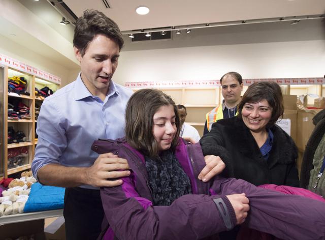 Justin Trudeau gives a Syrian refugee Sylvie Garabedian (C) a winter jacket as her mother Anjilik Jaghlassian looks on at the Pearson International airport, in Toronto. The first Canadian government plane carrying Syrian refugees arrived in Toronto. (The Canadian Press via AP)