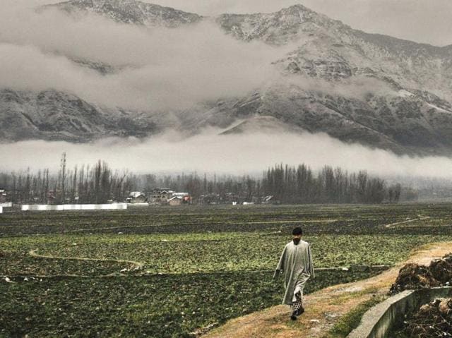A Kashmiri man walks as mountains stand covered with snow in the background, on the outskirts of Srinagar. (Waseem Andrabi/ HT Photo)