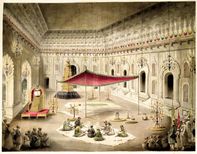Interior of the Imambara (in Lucknow) decorated as during the Muharram and the grave of Asaf al-Daula. The simple grave of Asaf al-Daula under a canopy inside the Imambara, with parties of imams reading the Koran, and a Ta’zia (model of a tomb) used during the Muharram procession beyond. Interior of the Imambara (in Lucknow) decorated as during the Muharram and the grave of Asaf al-Daula. The simple grave of Asaf al-Daula under a canopy inside the Imambara, with parties of imams reading the Koran, and a Ta’zia (model of a tomb) used during the Muharram procession beyond.