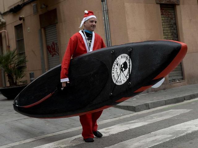 A person dressed as Santa Claus walks along a street with a paddle board to participate in a fund raiser at the beach in Barcelona. (AFP) A person dressed as Santa Claus walks along a street with a paddle board to participate in a fund raiser at the beach in Barcelona. (AFP)