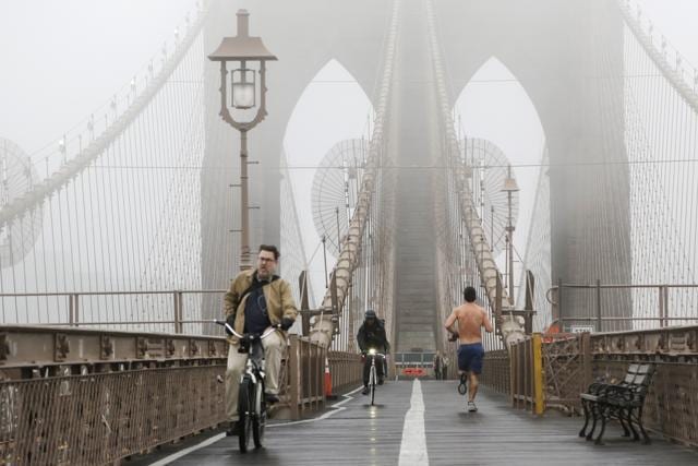 Bicyclists and a jogger cross the Brooklyn Bridge in heavy fog. (AP photo)