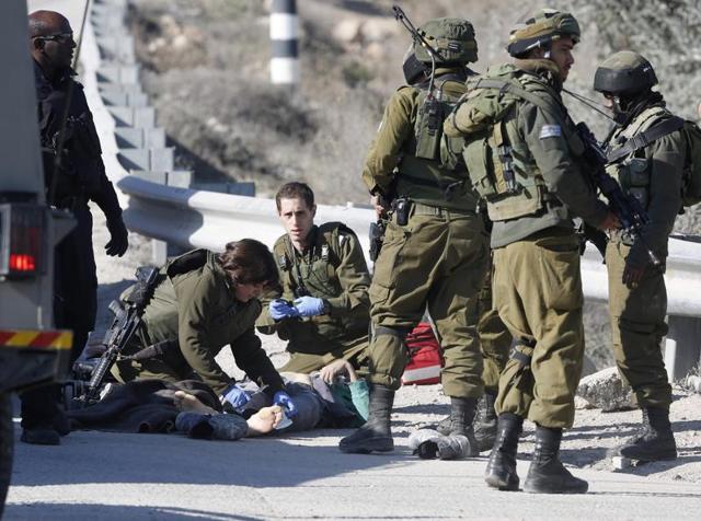 Israeli soldiers work around the body of a Palestinian assailant after he was shoot dead in the West Bank city of Hebron. (AP) Israeli soldiers work around the body of a Palestinian assailant after he was shoot dead in the West Bank city of Hebron. (AP)