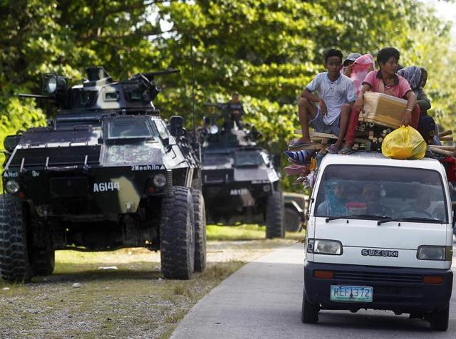 People drive past an armoured personnel carrier (APC) in Kauran, Ampatuan in the southern Philippines province of Maguindanao.Fourteen were killed, including nine Christian villagers, by Bangsamoro Islamic Freedom Fighter insurgents, while at least five rebels killed by government forces in clashes.(AFP)