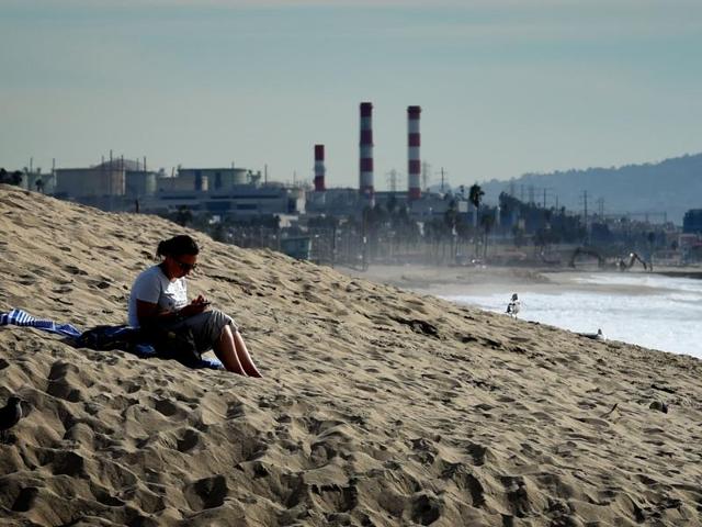A woman sits on a sand berm created by city workers to protect houses from El Nino storms and high tides in Los Angeles. After the world leaders reached the first truly universal climate pact, aimed at limiting average global warming to two degrees Celsius, the hard part now comes– following up on all the commitments.(AFP)
