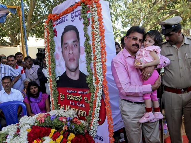 A relative carries Vismaya, daughter of India's National Security Guard commando Niranjan Kumar, portrait seen, who was among those killed in the attack on the Pathankot air force base, next to his coffin placed for public viewing, in Bangalore. (AP)