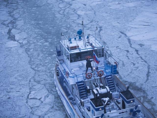 A crew member attaches a Russian national flag as the ice breaker moves along the frozen Moskva River with the Kremlin in the background during snowfall in Moscow, Russia. (AP)
