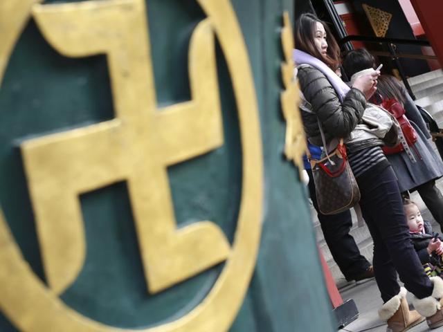 Visitors stand next to a religious ornament with the "manji" symbol, which is widely used to denote Buddhist temples on maps and elsewhere, at a temple in Tokyo.(AP)