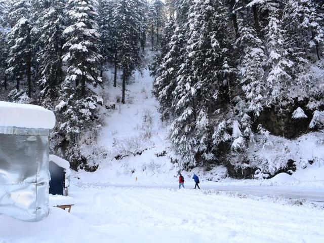 Two people walking on the snow covered road at Kufri after heavy snowfall in Shimla on Monday. (Deepak Sansta/HT Photo)