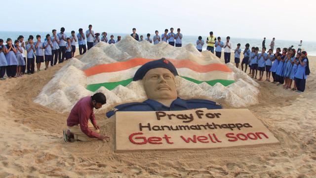 Renowned sand artist Sudarsan Pattnaik creates a sand sculpture of Lance Naik Hanumanthappa Koppad for his speedy recovery at Puri sea beach on Wednesday. (PTI Photo)