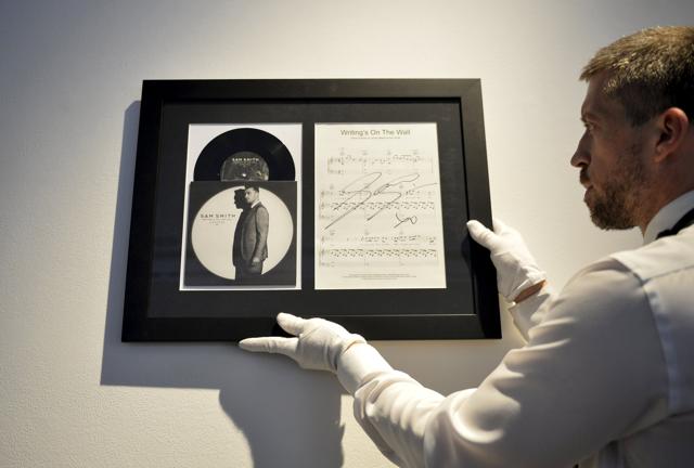 An employee holds a signed Sam Smith Writing's on the Wall sheet music framed with a 45rpm 7" vinyl single and sleeve from the James Bond film Spectre. (REUTERS) An employee holds a signed Sam Smith Writing's on the Wall sheet music framed with a 45rpm 7" vinyl single and sleeve from the James Bond film Spectre. (REUTERS)