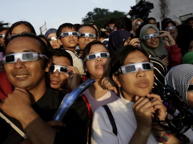 People look up at the sun wearing protective glasses to watch the eclipse in Jakarta, Indonesia. The rare astronomical event is being witnessed along a narrow path that stretches across 12 provinces encompassing three times zones and about 40 million people. (AP)