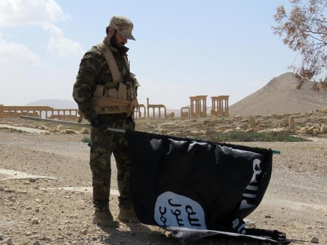 A member of the Syrian pro-government forces carries an Islamic State (IS) group flag as he stands on a street in the ancient city of Palmyra on Sunday after troops recaptured the city from IS jihadists. (AFP) A member of the Syrian pro-government forces carries an Islamic State (IS) group flag as he stands on a street in the ancient city of Palmyra on Sunday after troops recaptured the city from IS jihadists. (AFP)