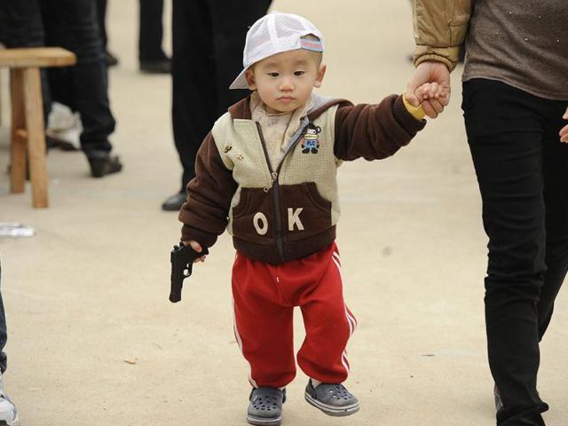 A child walks with his toy gun walks with his mother. A Chinese expert has warned that 100 million children from migrant labourers have been left behind in the country. A child walks with his toy gun walks with his mother. A Chinese expert has warned that 100 million children from migrant labourers have been left behind in the country.