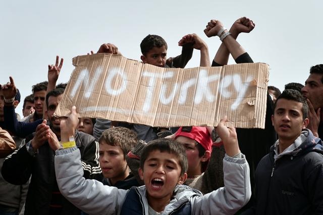 Refugees and migrants including children who left the Chios registration camp, shout slogans and hold placards reading "'No Turkey" as they camp out in the port of Chios. (AFP)