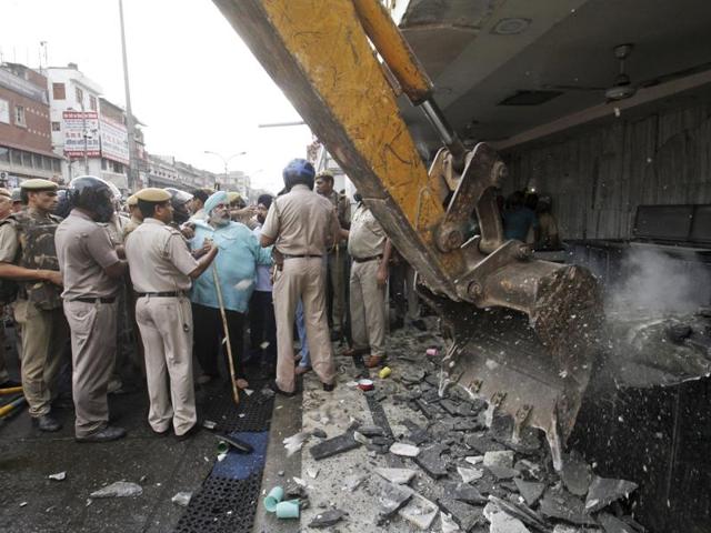 Policemen talk to locals as a crane removes an illegal structure.  (Sanchit Khanna/HT Photo) 