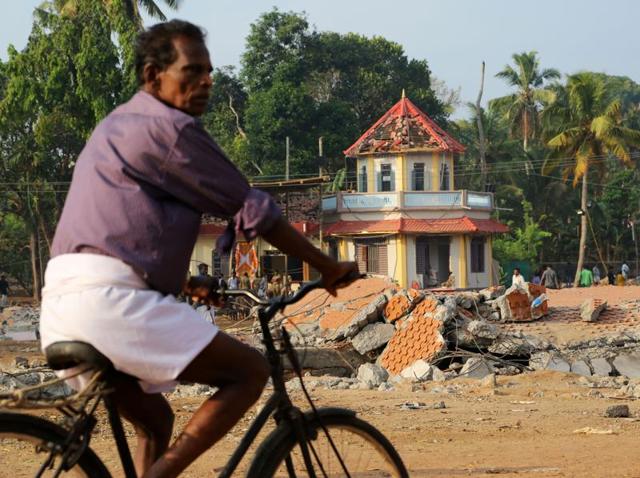 A cyclist rides past damaged structures at the spot where a massive fire broke out during a fireworks display at the Puttingal temple complex in Paravur village, Kollam district. (AP) A cyclist rides past damaged structures at the spot where a massive fire broke out during a fireworks display at the Puttingal temple complex in Paravur village, Kollam district. (AP)