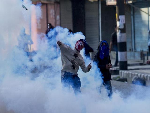 A masked Kashmiri Muslim protester throws back an exploded tear gas shell at policemen during a protest in Srinagar on Tuesday. Four have been killed in firing by security forces at stone-pelters in Handwara. (AP) 