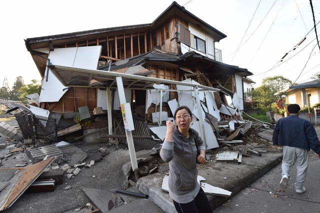 A couple heads to their home past a collapsed house in Mashiki. (AFP)